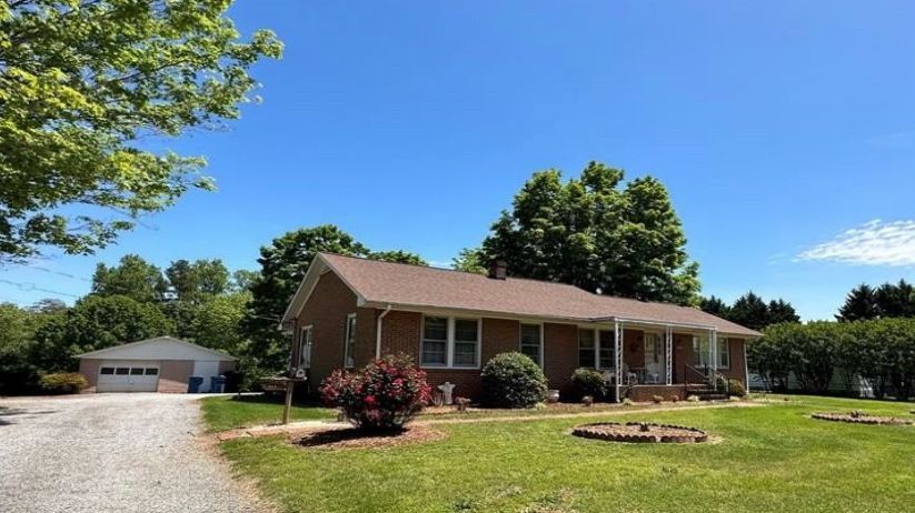 A ranch-style house with a gravel driveway, detached garage, and blue sky.