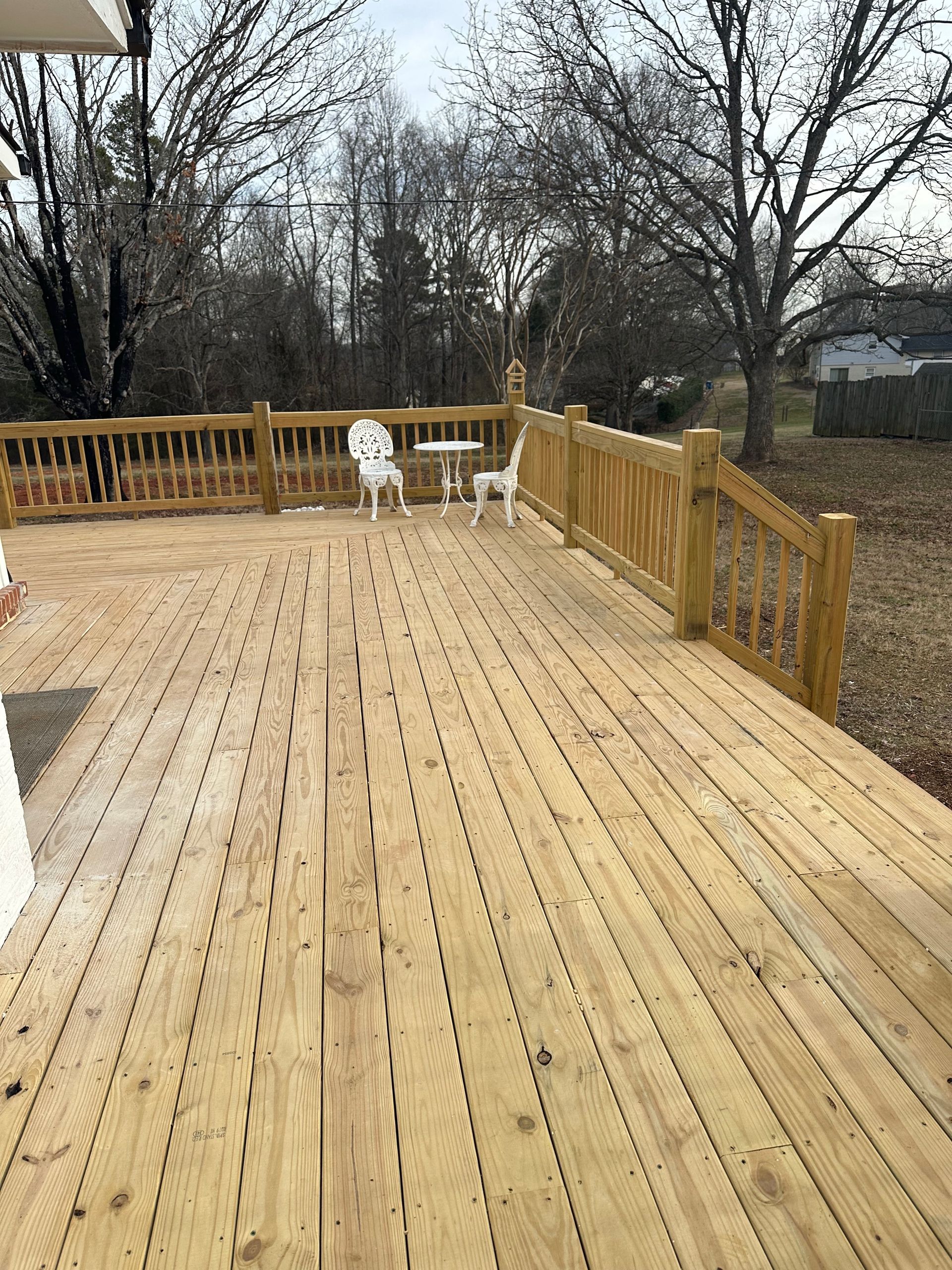 Wooden deck with railing, two white chairs, and small table; outdoor setting.