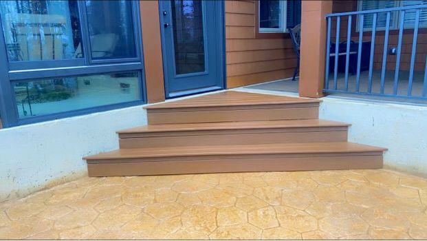 Three wooden steps leading up to a door, on a patterned concrete patio.