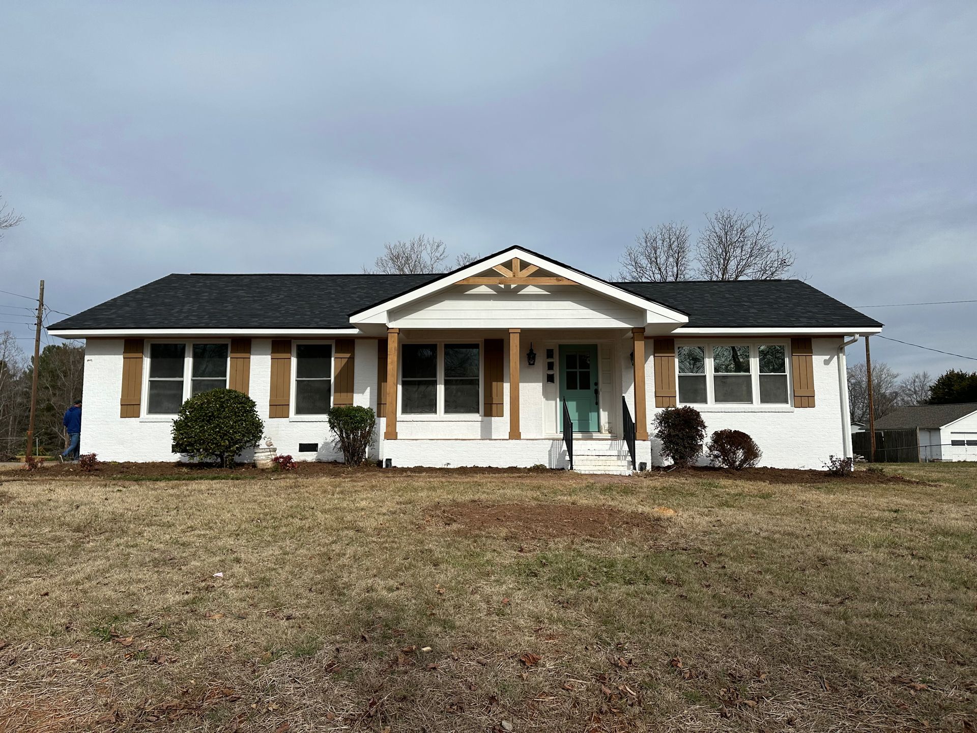 White house with dark roof and brown shutters under a cloudy sky.
