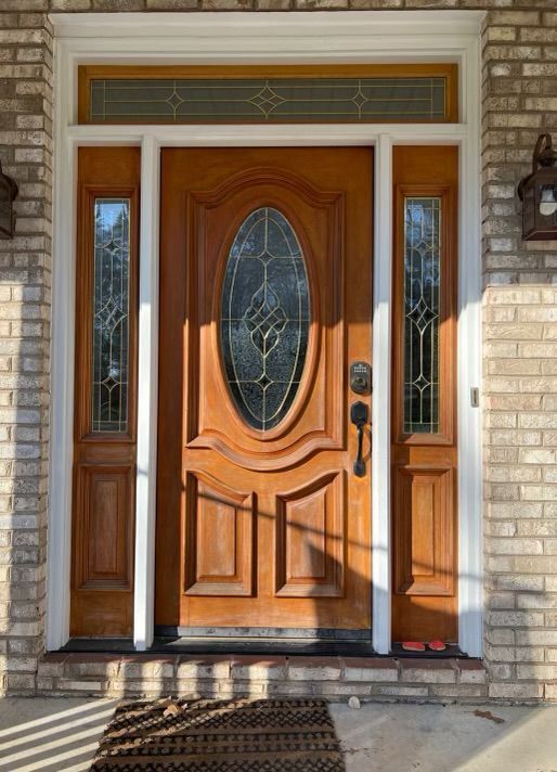 Wooden front door with sidelights, oval glass window, white trim, brick facade.