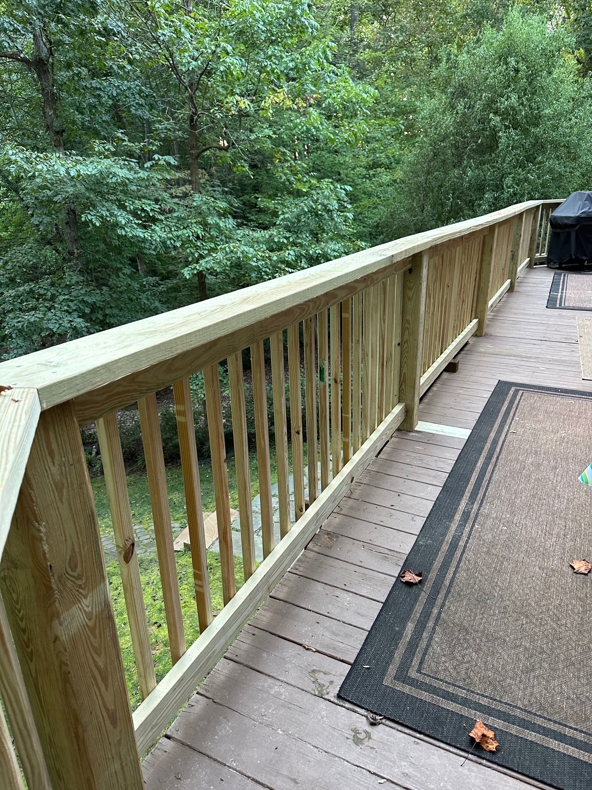 Wooden deck with railing overlooking a wooded area.