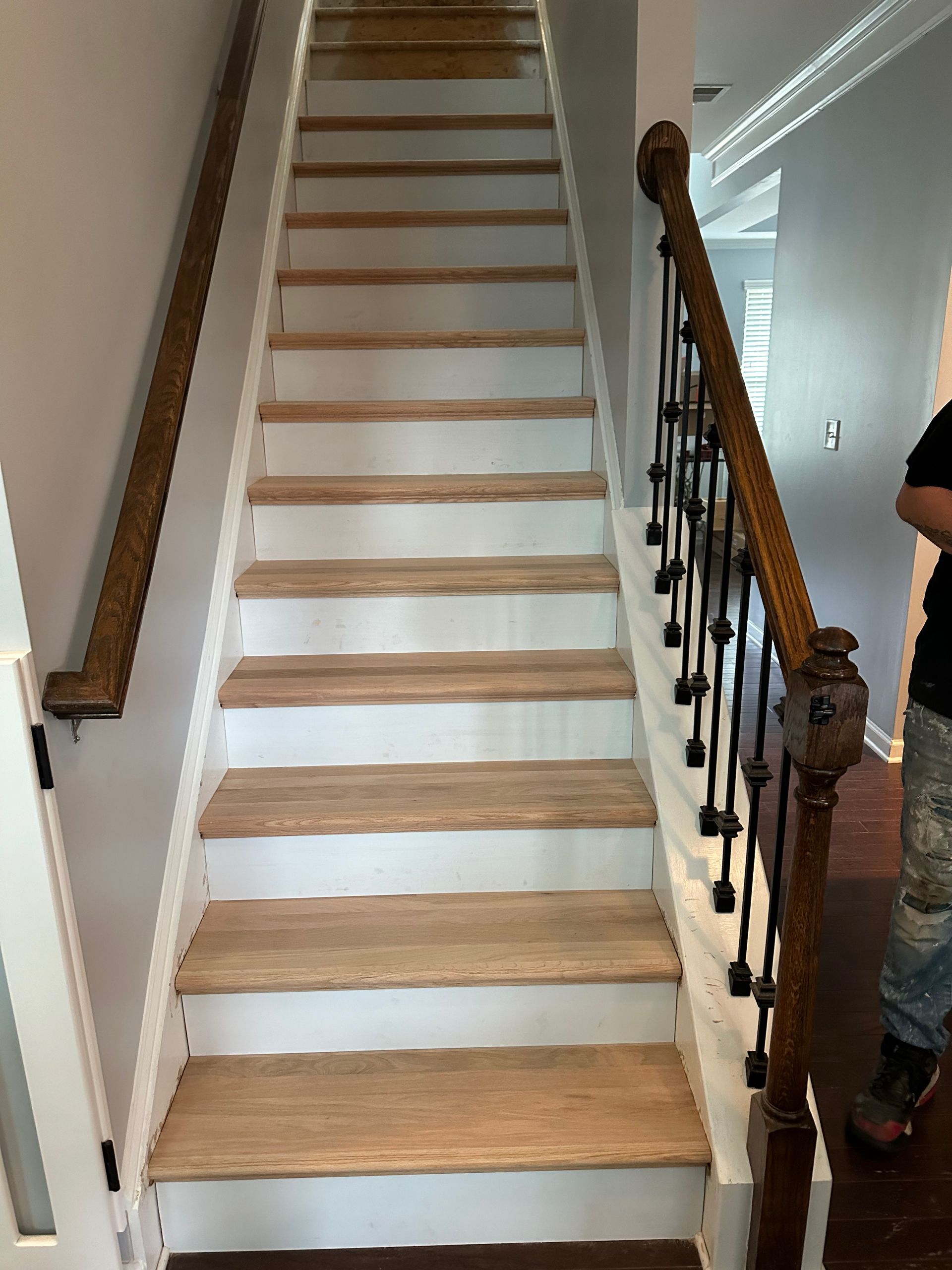 Wooden staircase with white risers, brown handrails, and dark metal balusters. A person stands nearby.