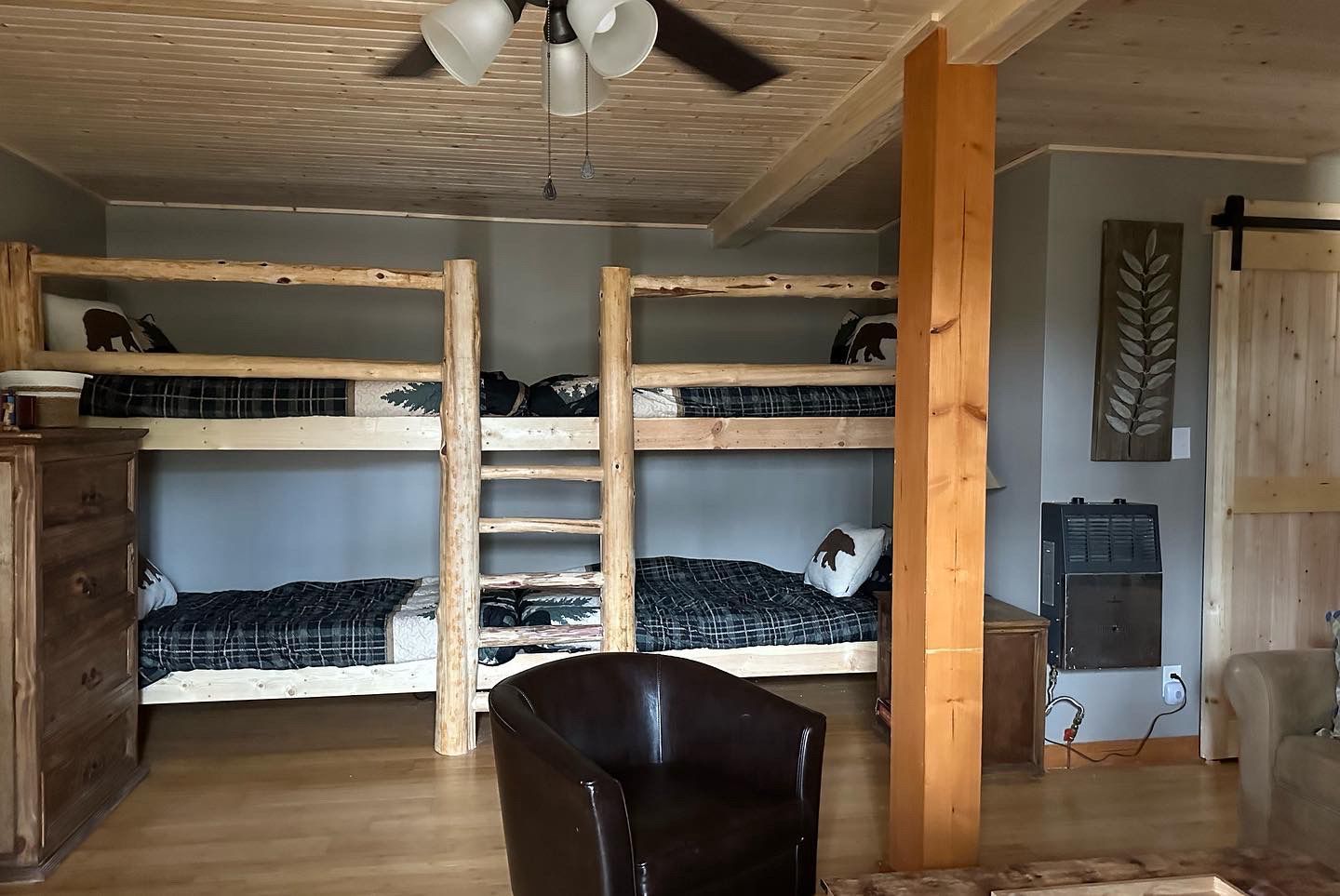 Bedroom with two wooden bunk beds, wooden support beam, dark leather armchair, wooden door with sliding track.