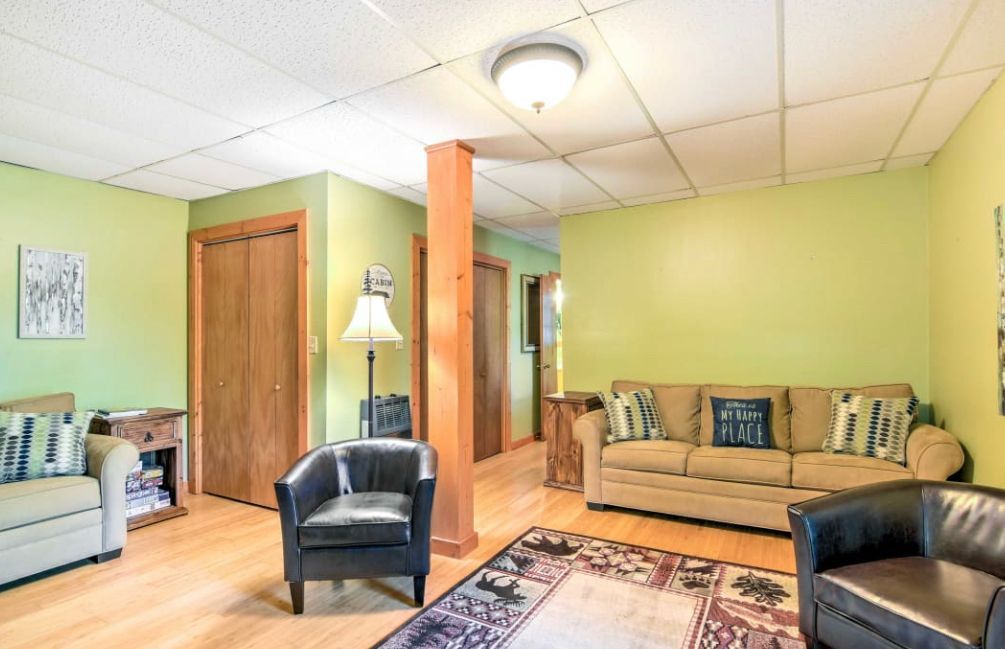 Living room with lime green walls, beige sofa, black chairs, wooden floors, and a brown pillar.