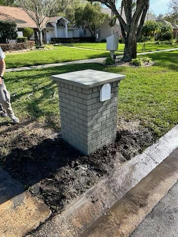 Brick mailbox with gray cap, white mail slot, in front yard next to street.