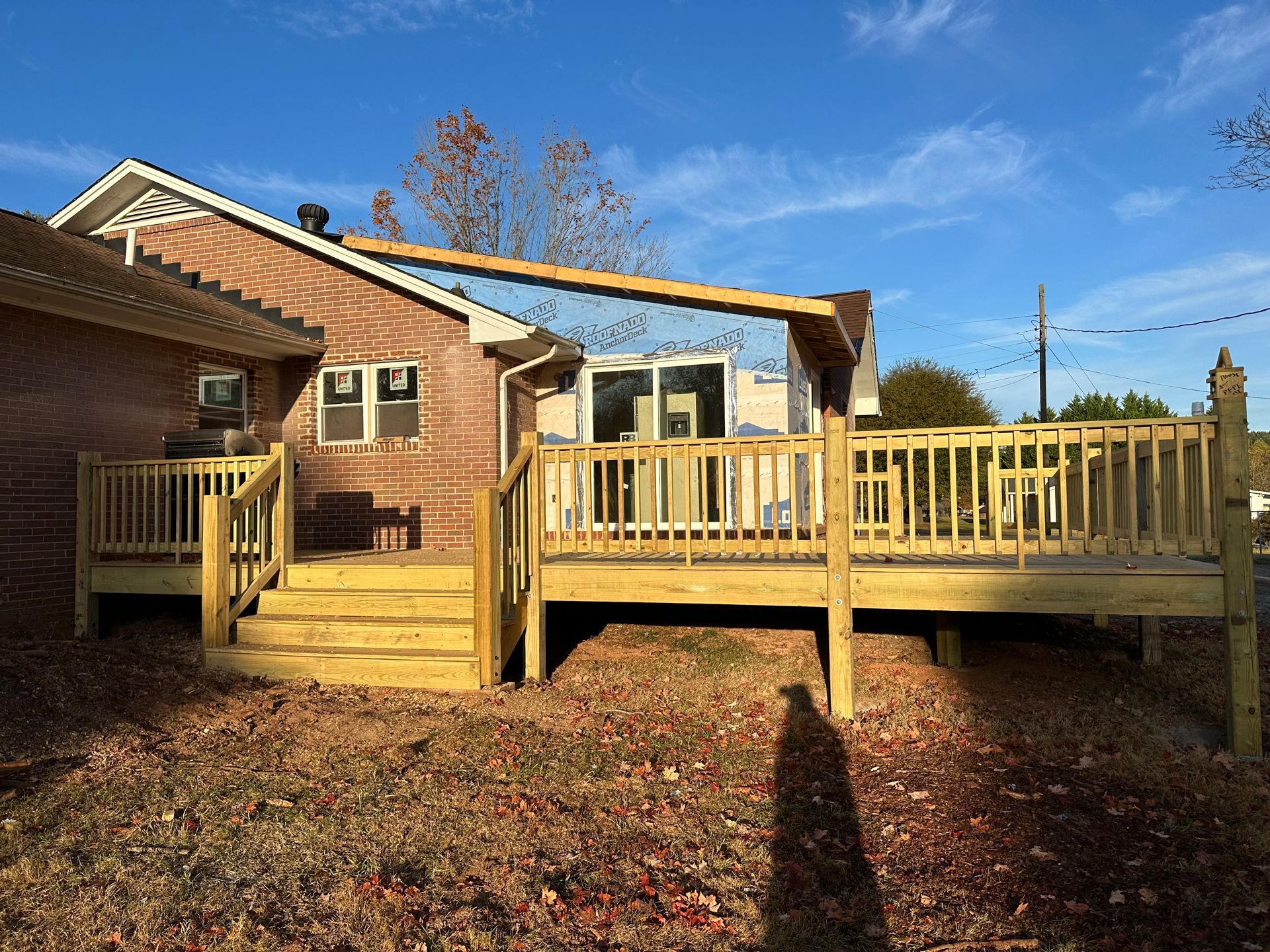 Wooden deck with steps, connected to a brick building, under a blue sky.