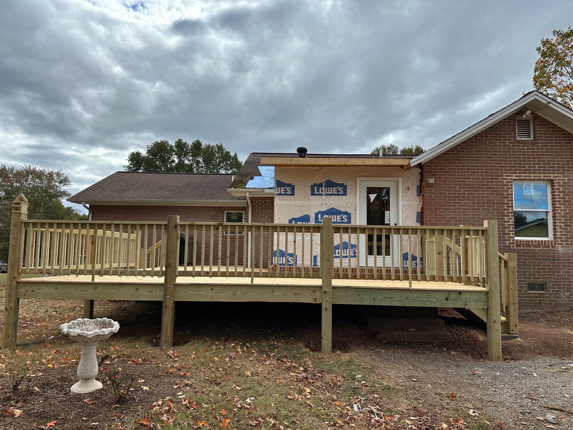 Wooden deck attached to a brick house under construction, cloudy sky above.