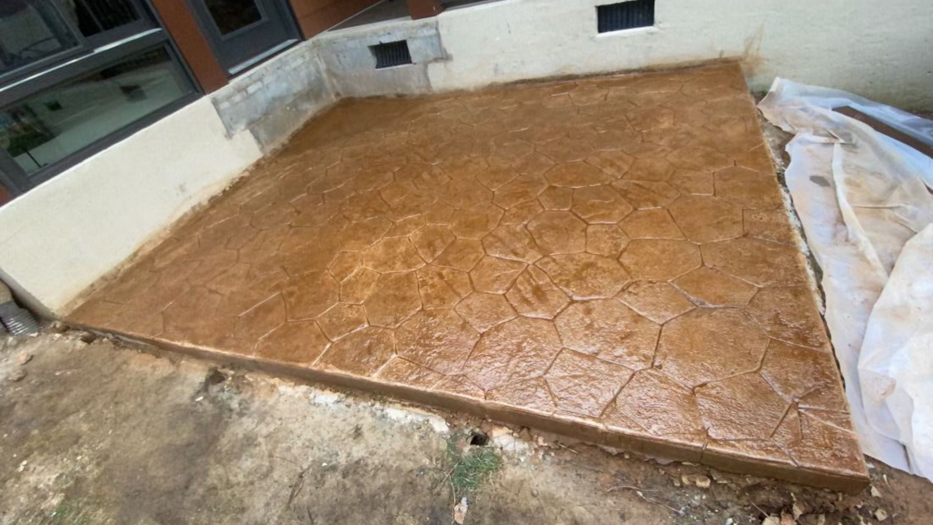 Brown stamped concrete patio, textured to resemble stone, near building exterior.