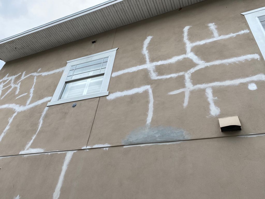 Tan house with stone facade, dark roof, green lawn, trees, and driveway.