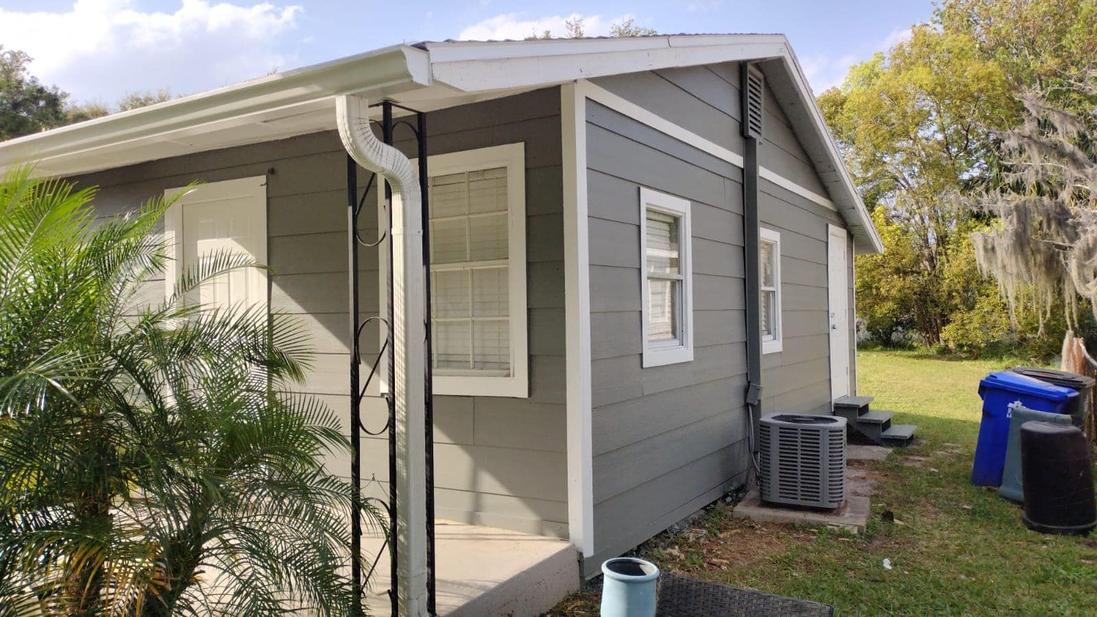 Person patching a wall inside a room with a wooden ceiling and window. Tools and materials are on the floor.