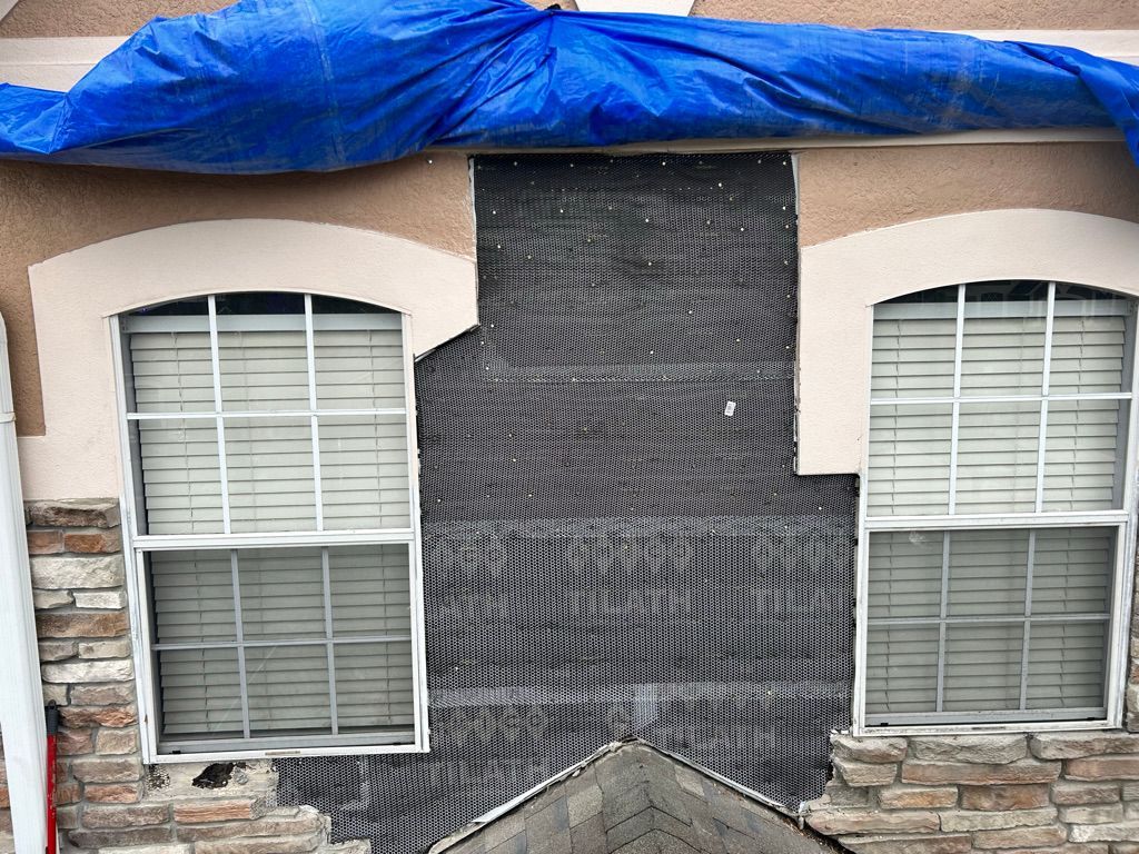 Tan house with stone facade, dark roof, green lawn, trees, and driveway.