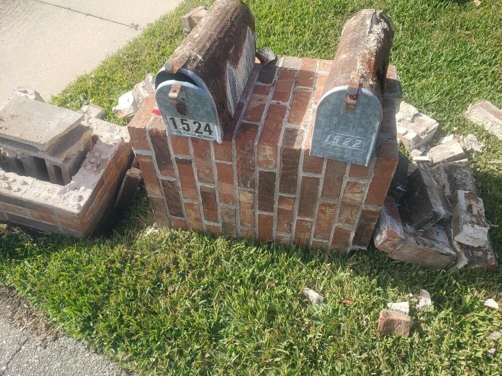Tan house with stone facade, dark roof, green lawn, trees, and driveway.