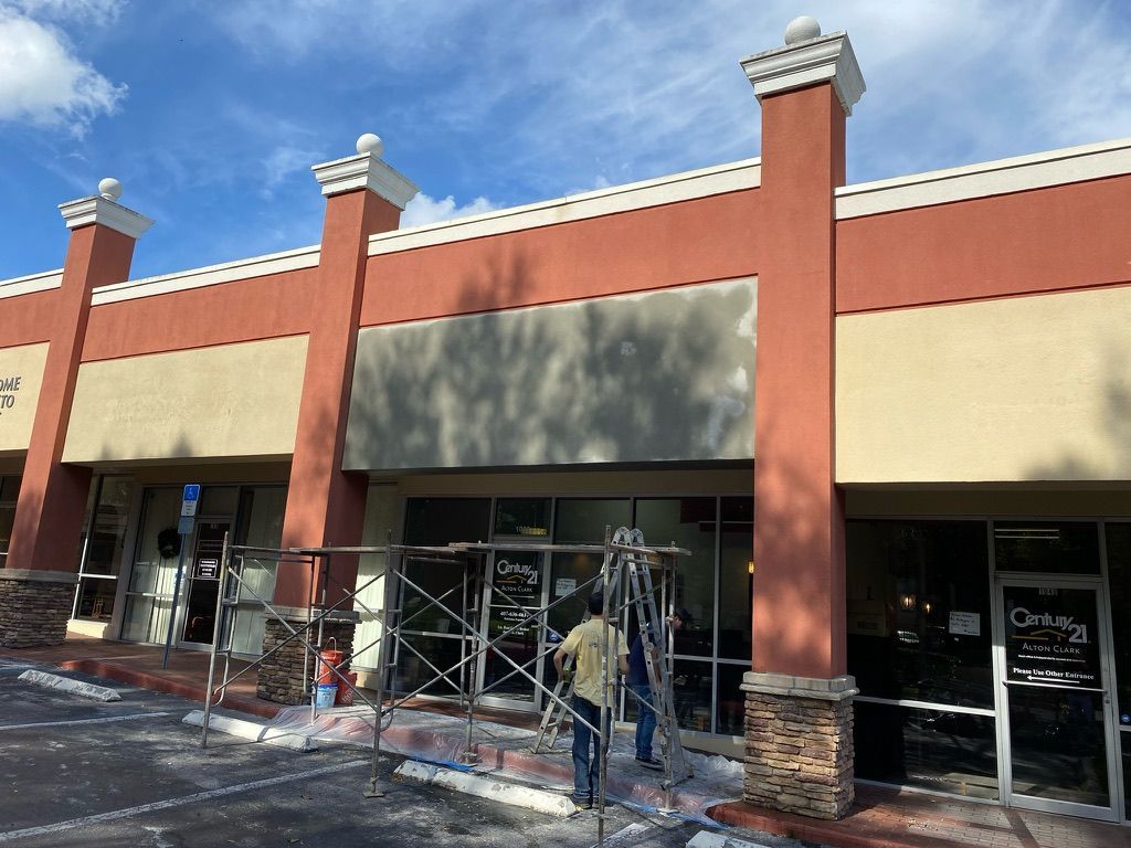 Tan house with stone facade, dark roof, green lawn, trees, and driveway.