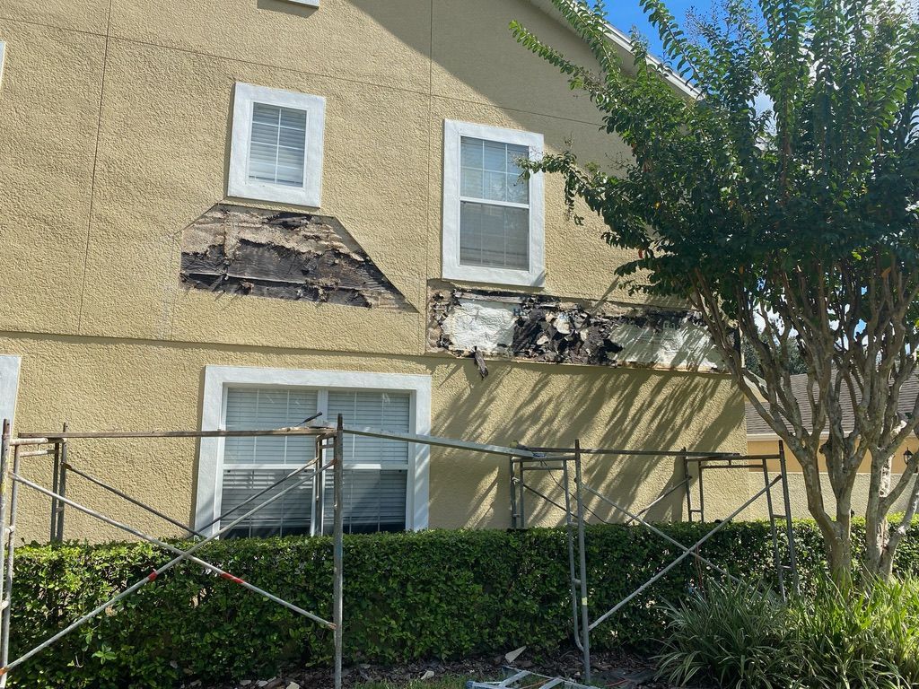 Person patching a wall inside a room with a wooden ceiling and window. Tools and materials are on the floor.