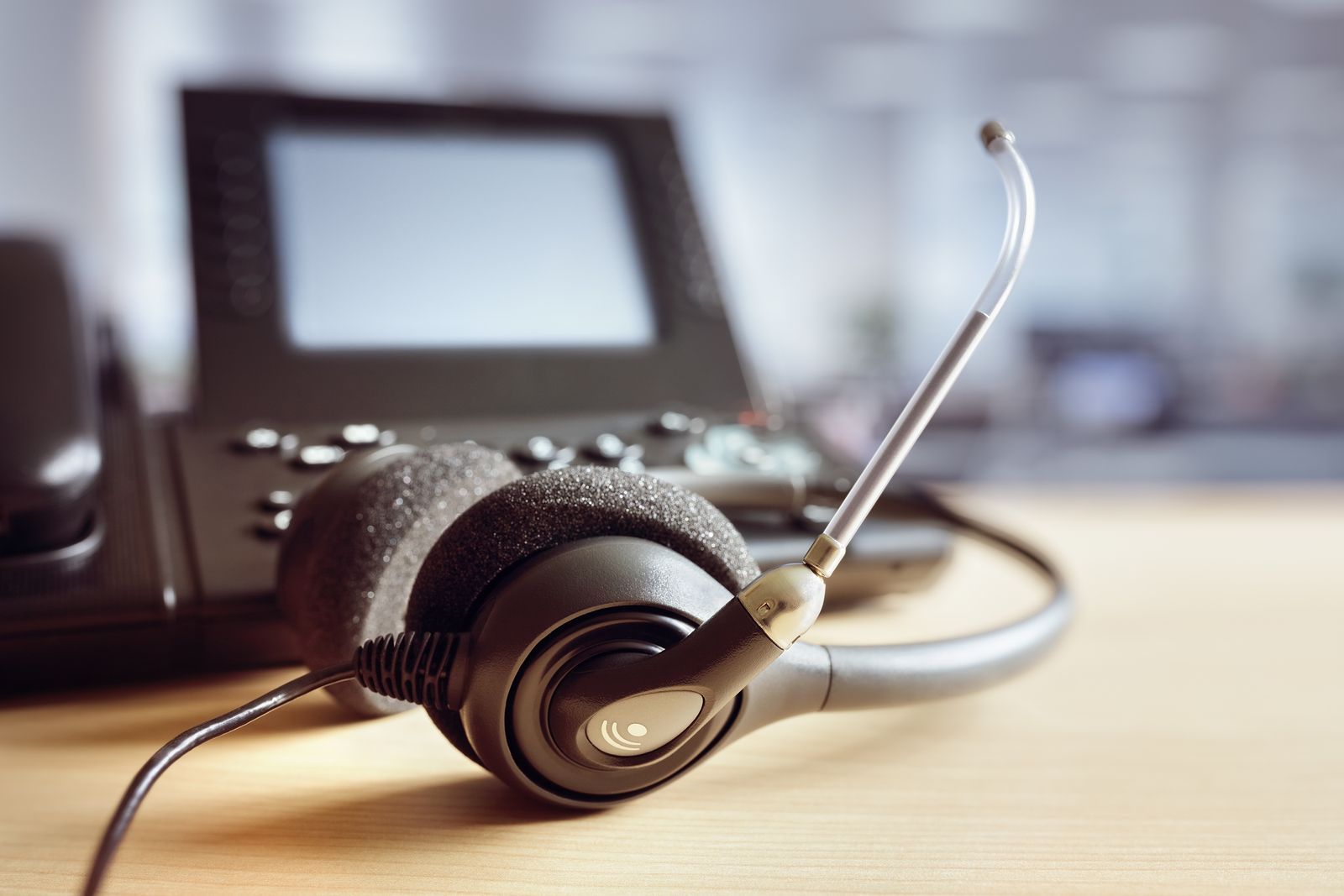 A headset is sitting on a desk next to a telephone.