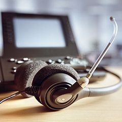 A headset is sitting on a wooden table next to a telephone.