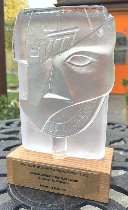 A glass sculpture of a face is sitting on a wooden base on a table.