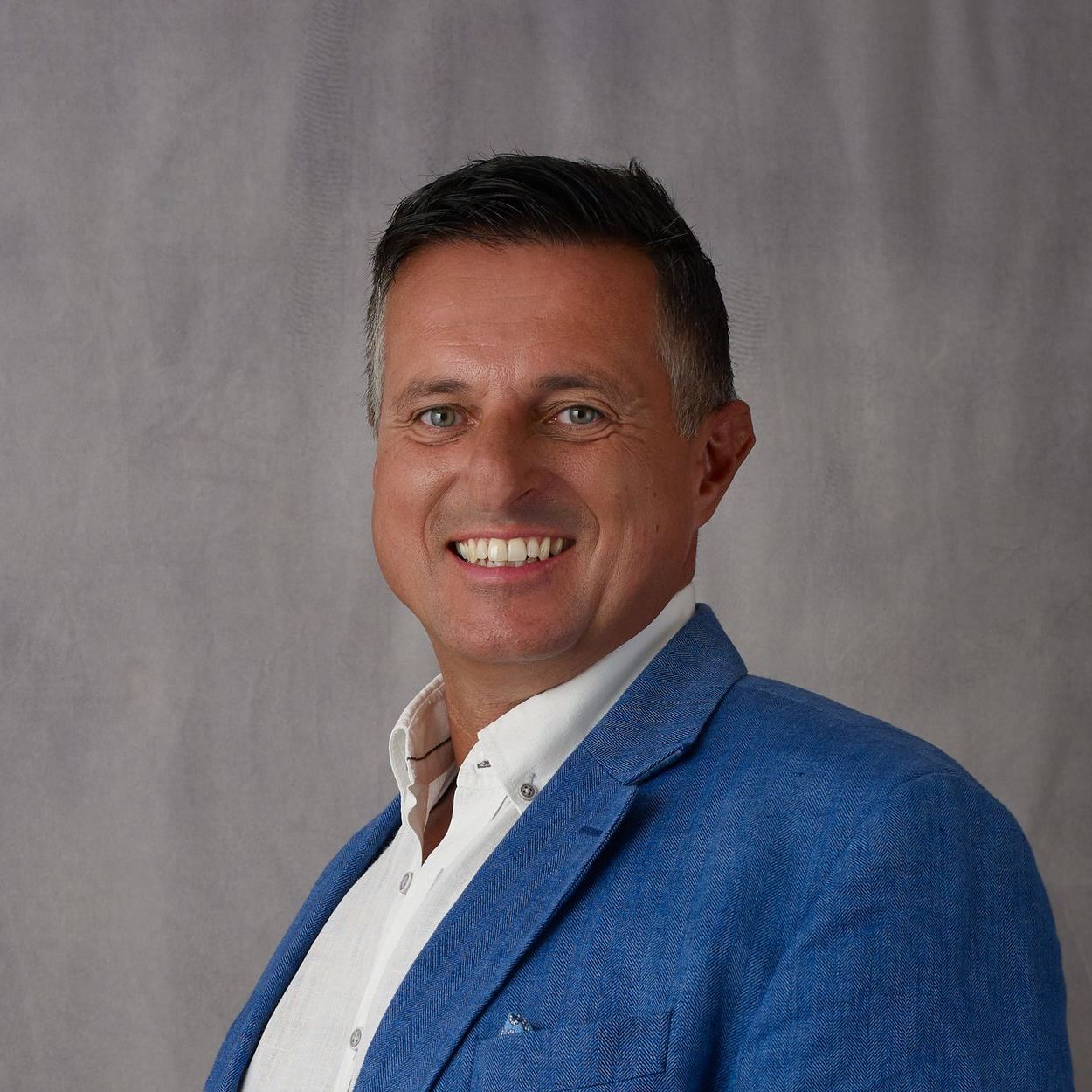 A man wearing a blue jacket and white shirt is smiling for the camera.