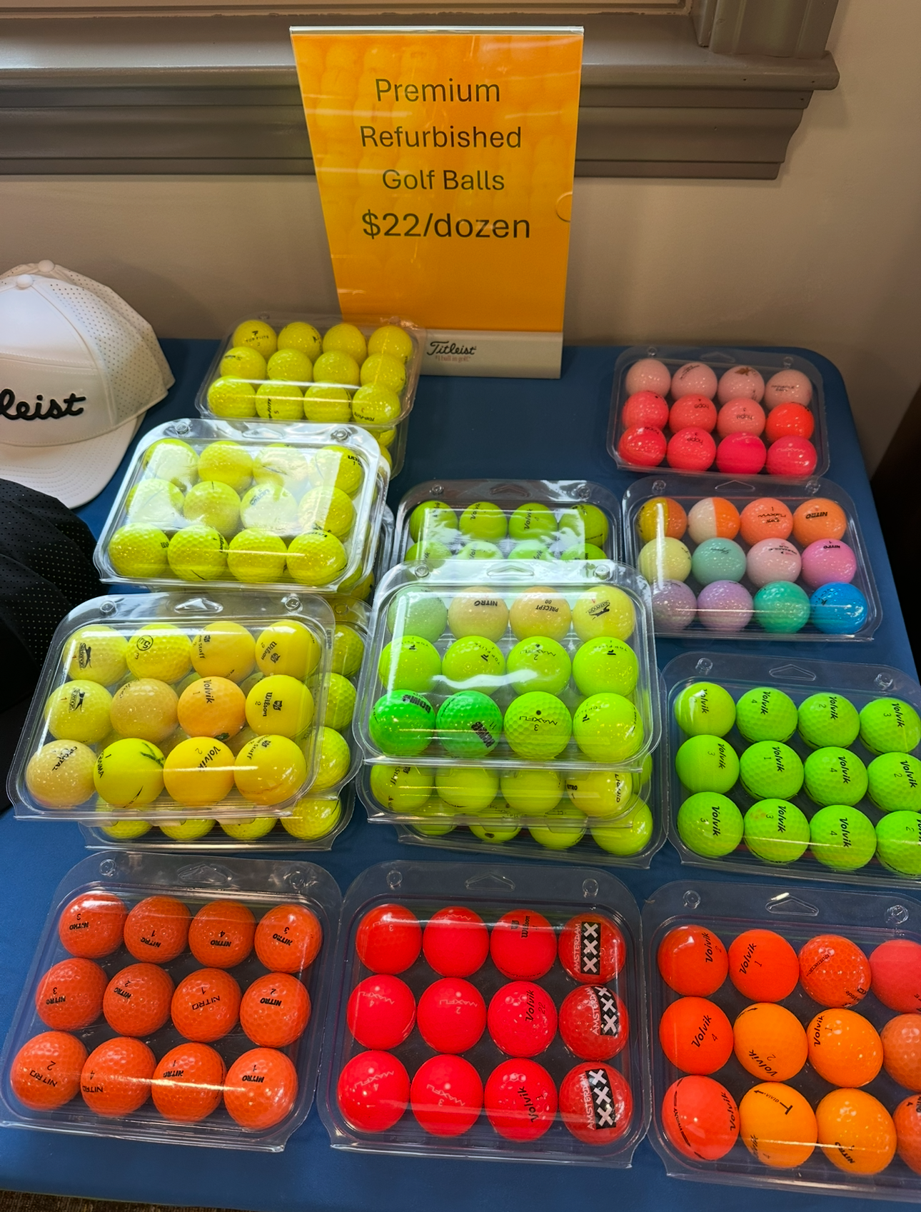 A bunch of golf balls on a table with a sign that says premium refurbished golf balls $ 22 / dozen