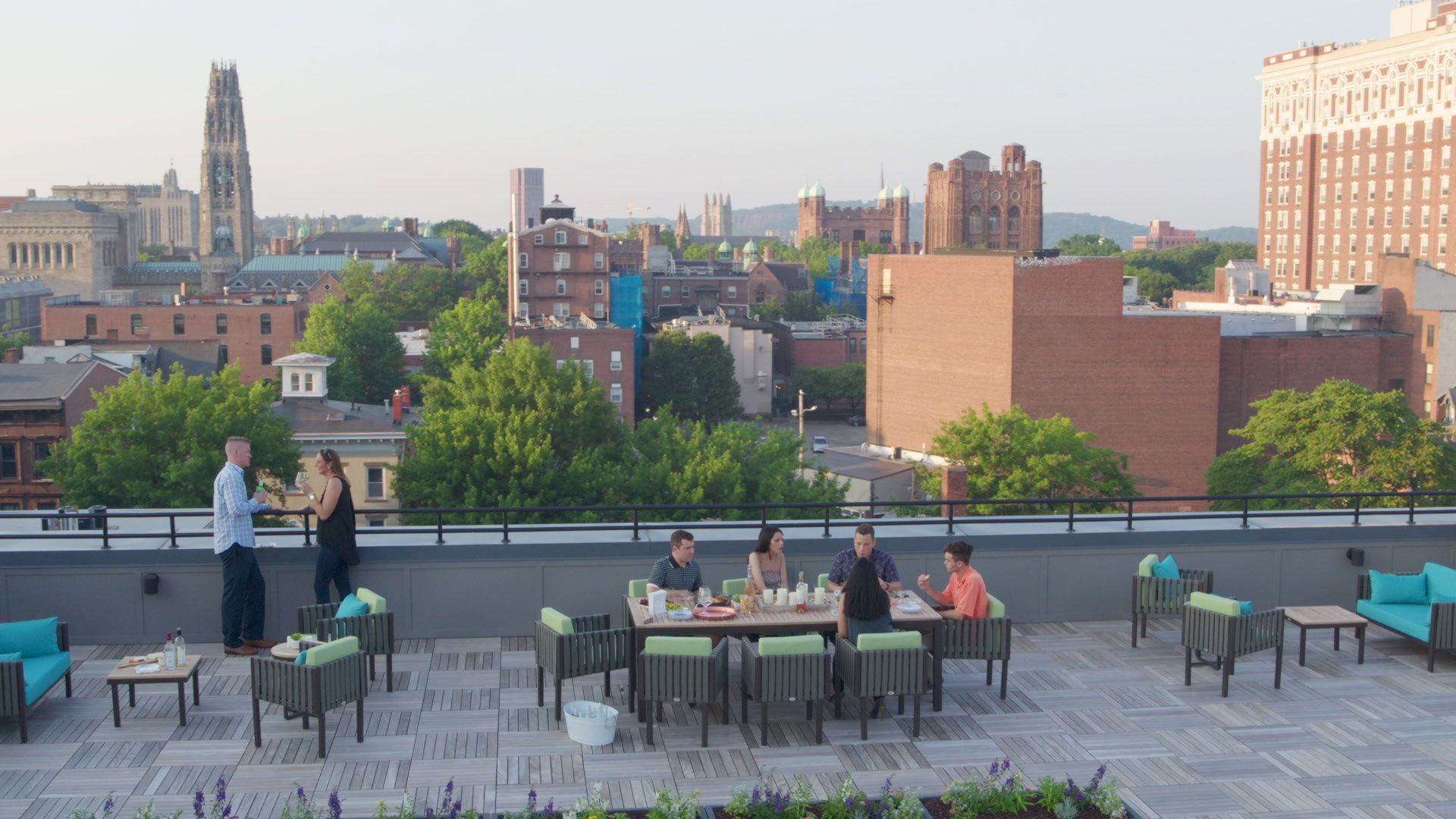 A group of people are sitting at a table on a rooftop overlooking a city.