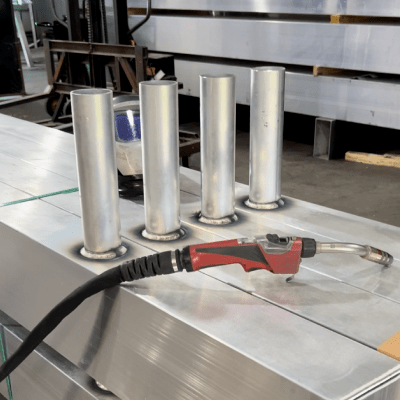 Four metal tubes welded to a flat aluminum surface, with a welding torch in the foreground.