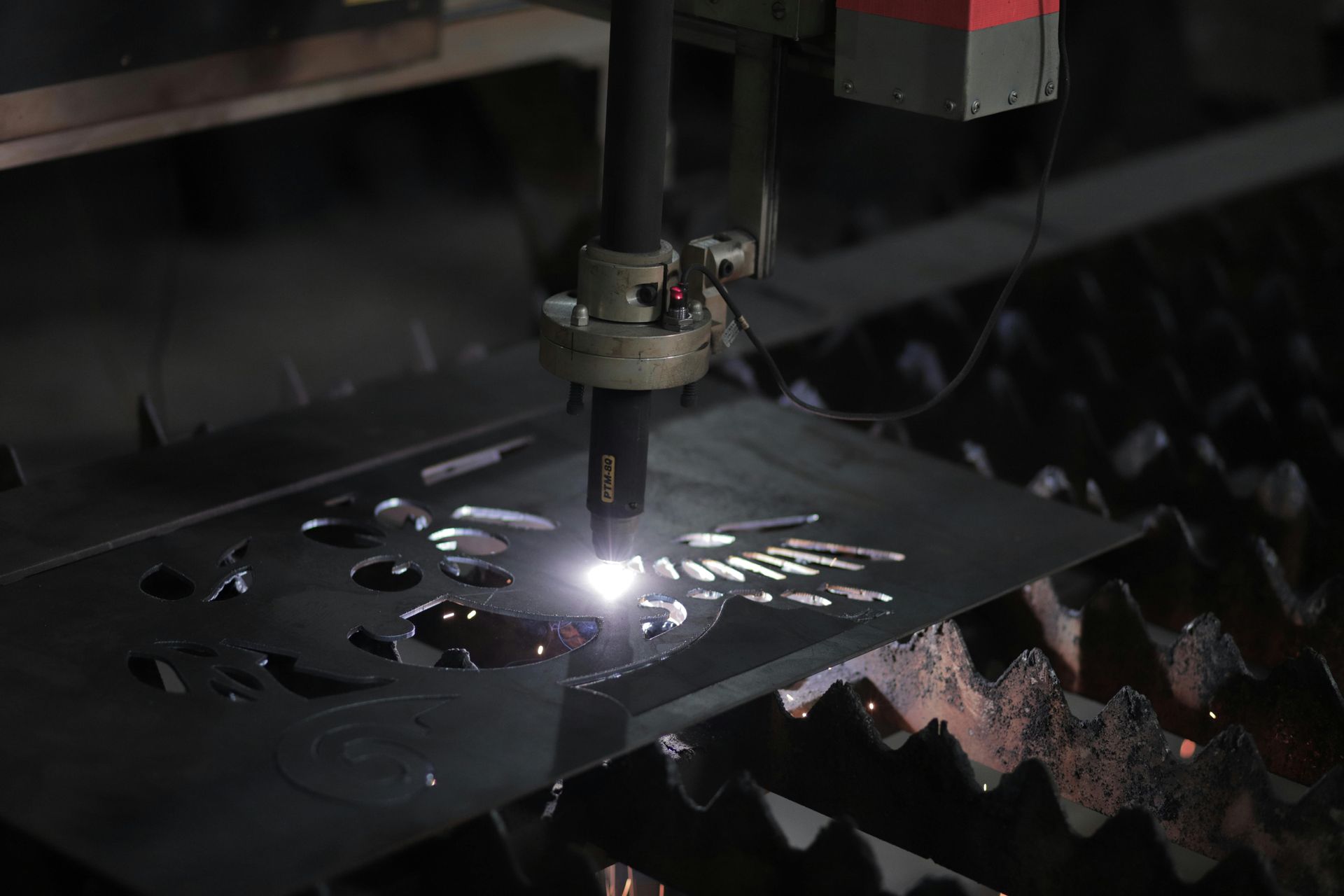 Laser cutting black metal sheet, with bright sparks in an industrial machine.
