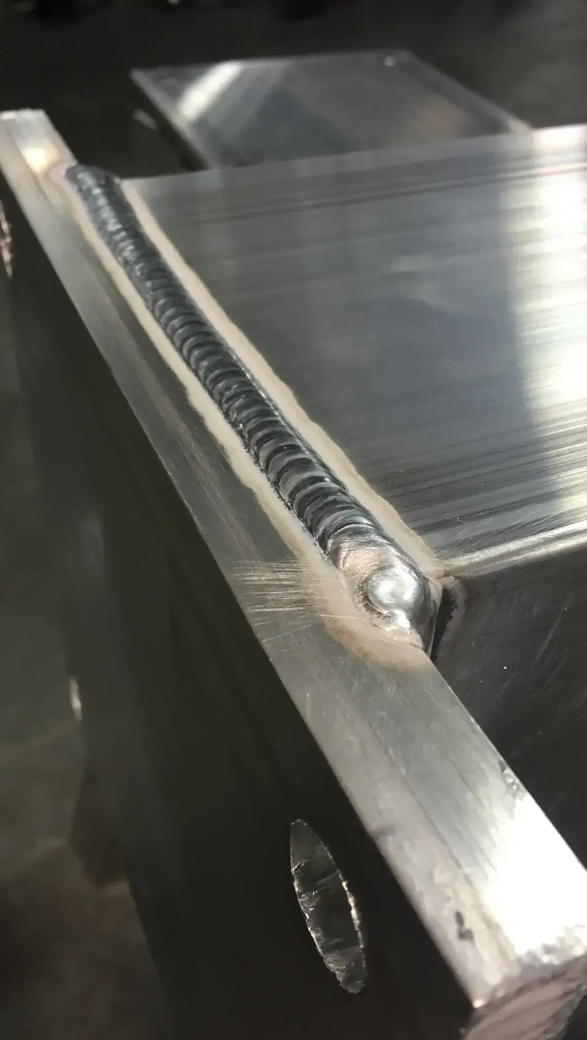 Close-up of a silver metal weld on a rectangular structure. The weld is a line of small, connected bumps.