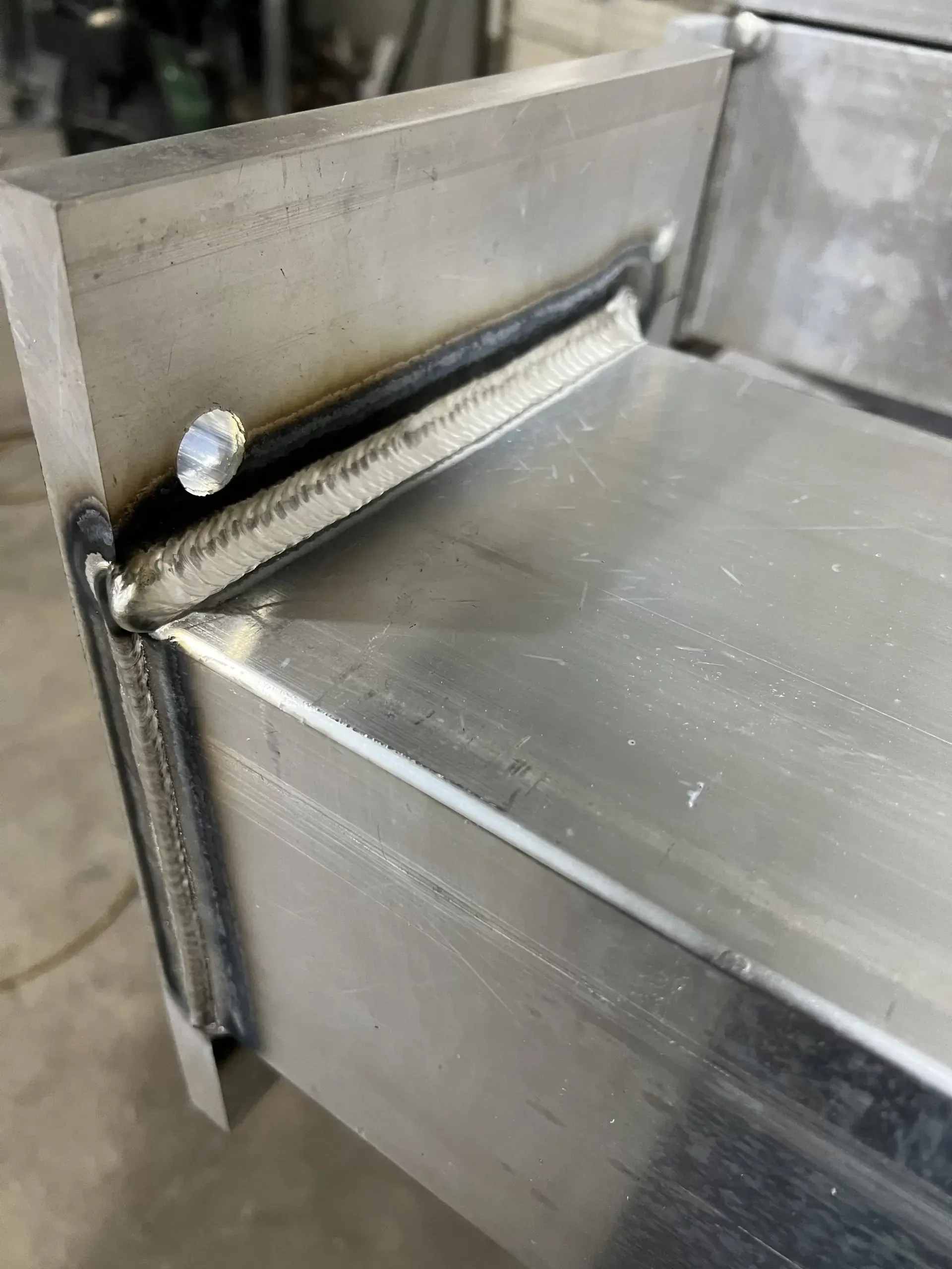 Metal box corner with welded seams and a bolt.