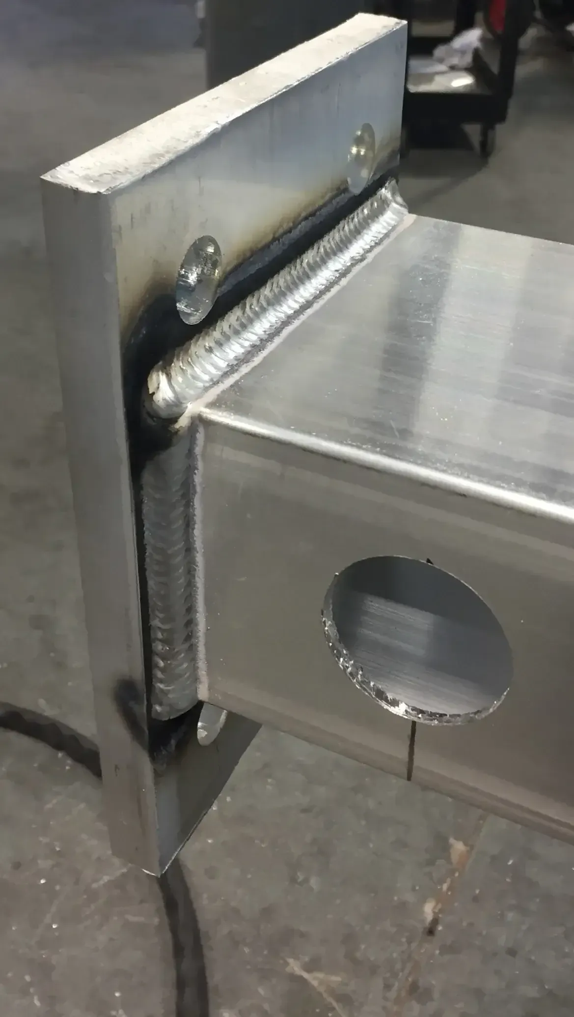 Close-up of welded aluminum frame with a large hole and a mounting plate attached by bolts.