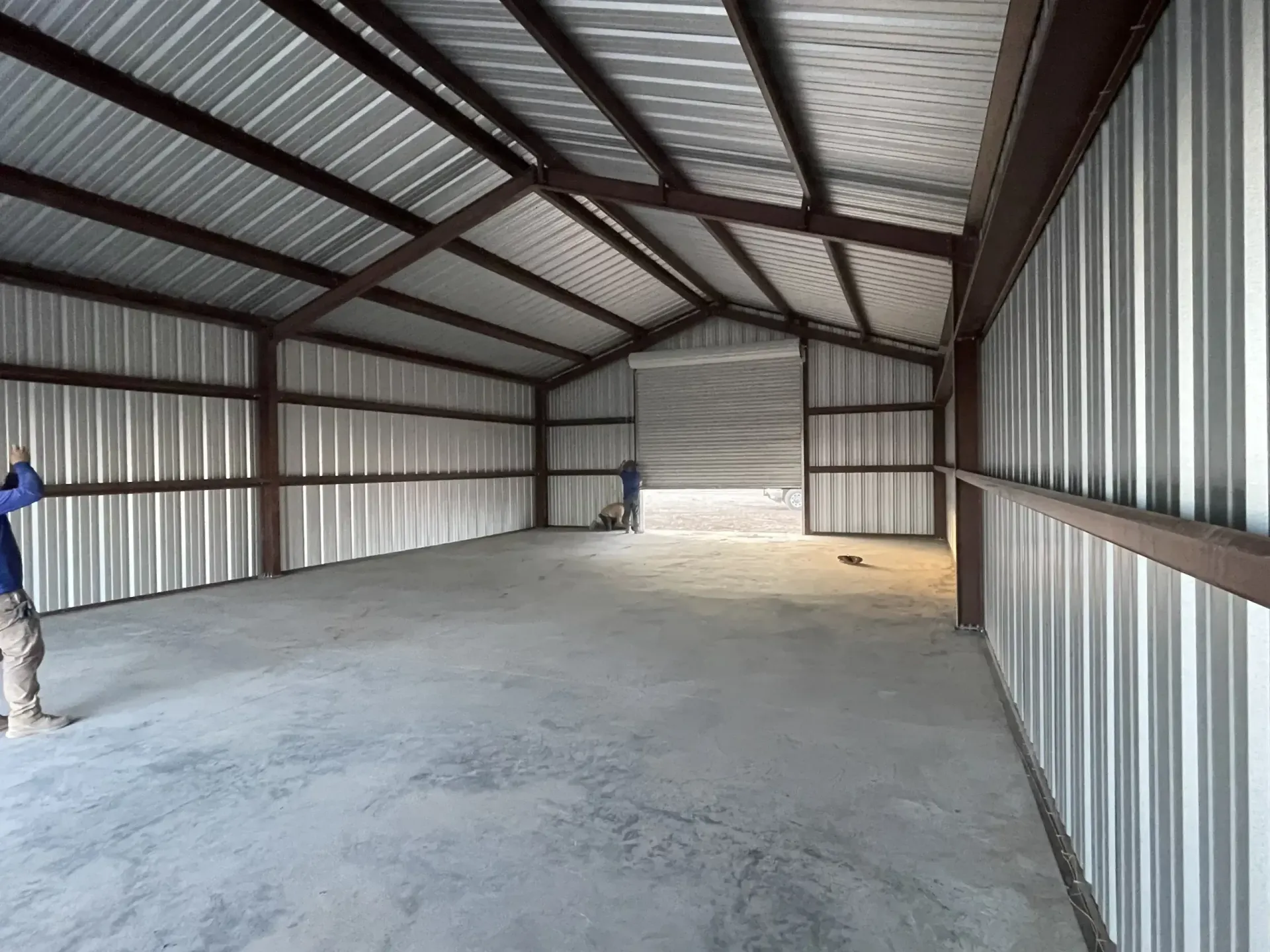 Interior of a metal building with brown beams and corrugated metal walls and ceiling. Concrete floor.