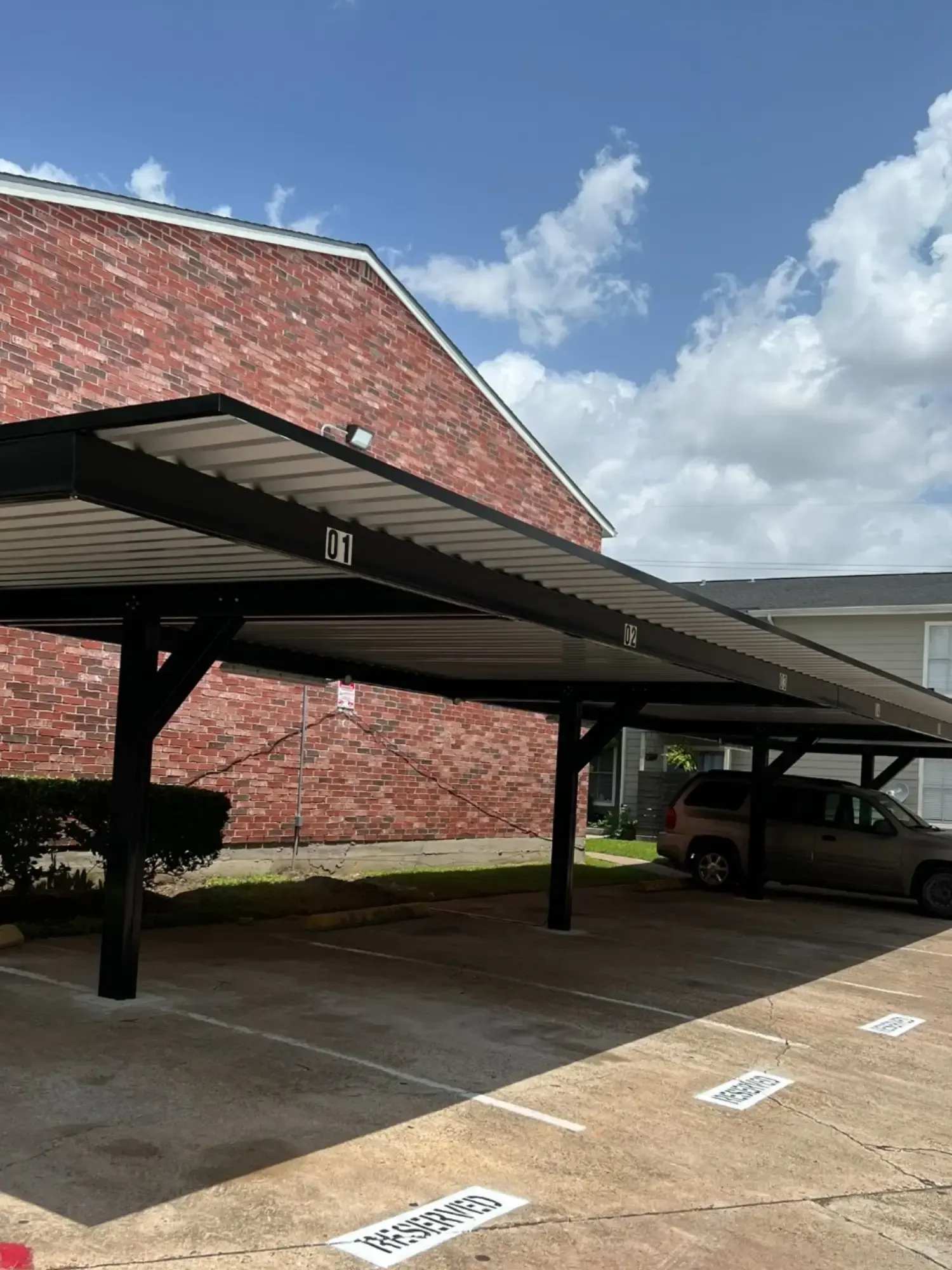 Carport with parked car, against a brick building and blue sky.