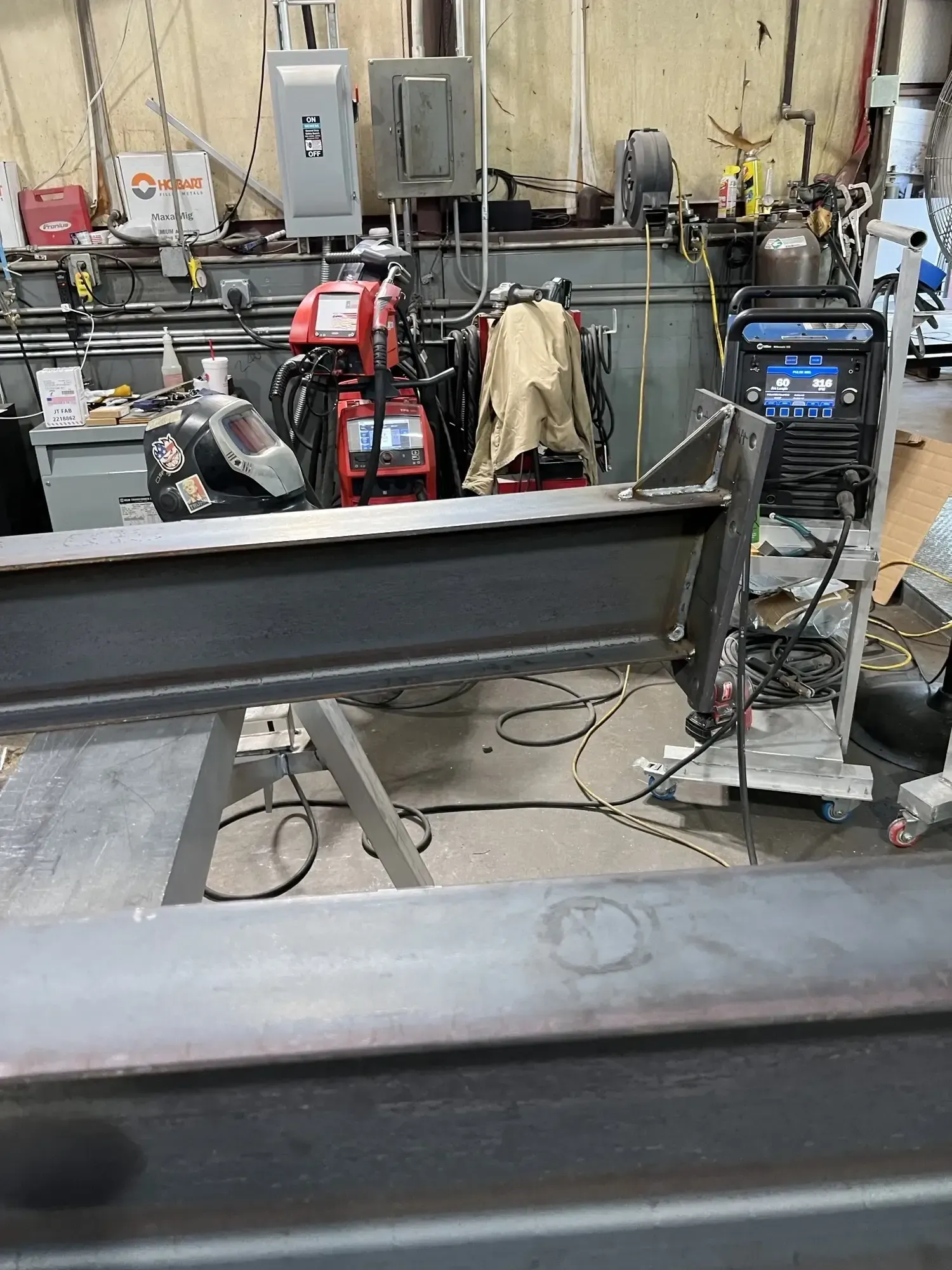 Welding shop scene with metal beams, welding machines, and equipment.