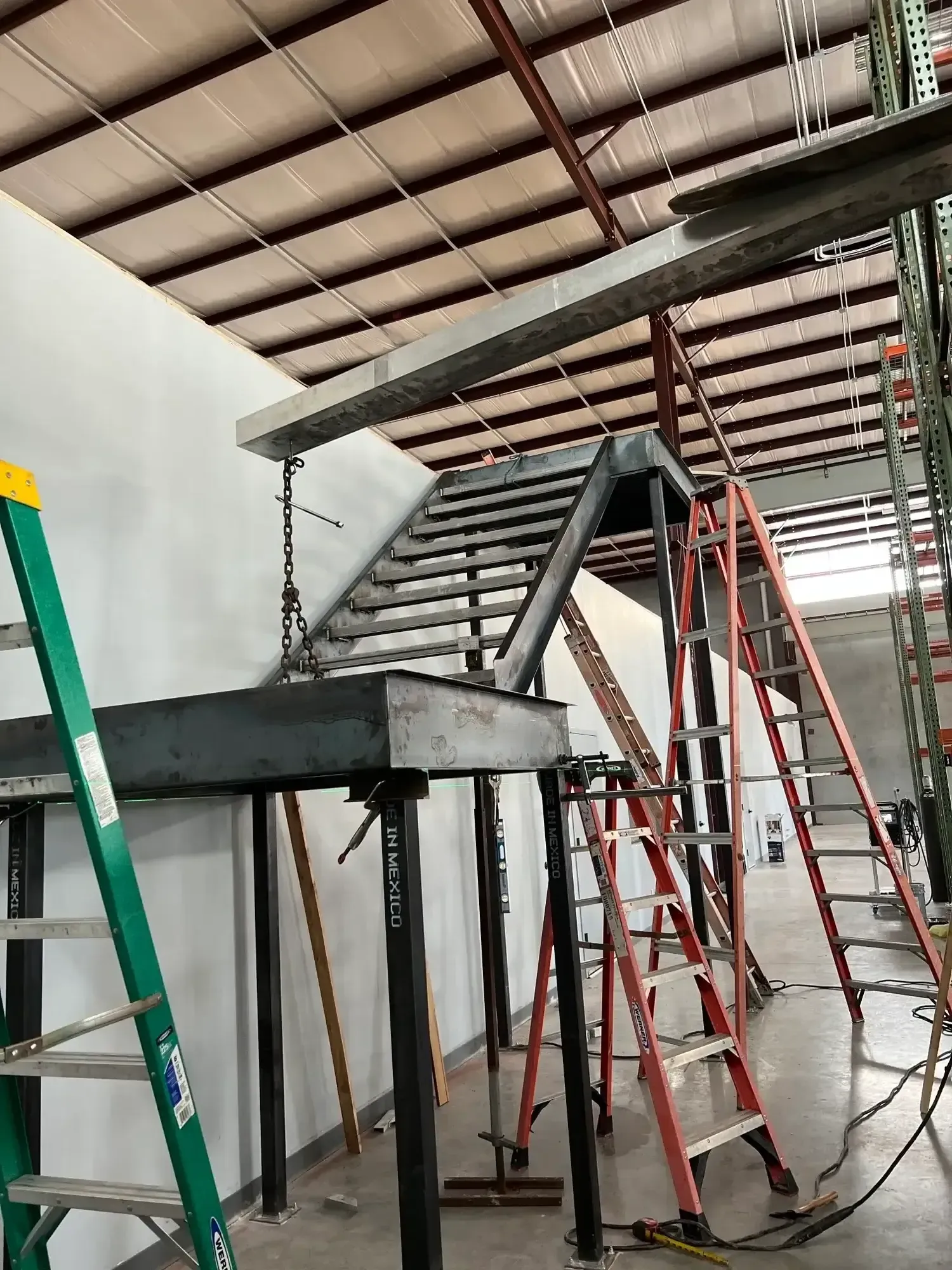 Warehouse interior with metal stairs under construction; multiple ladders are present.