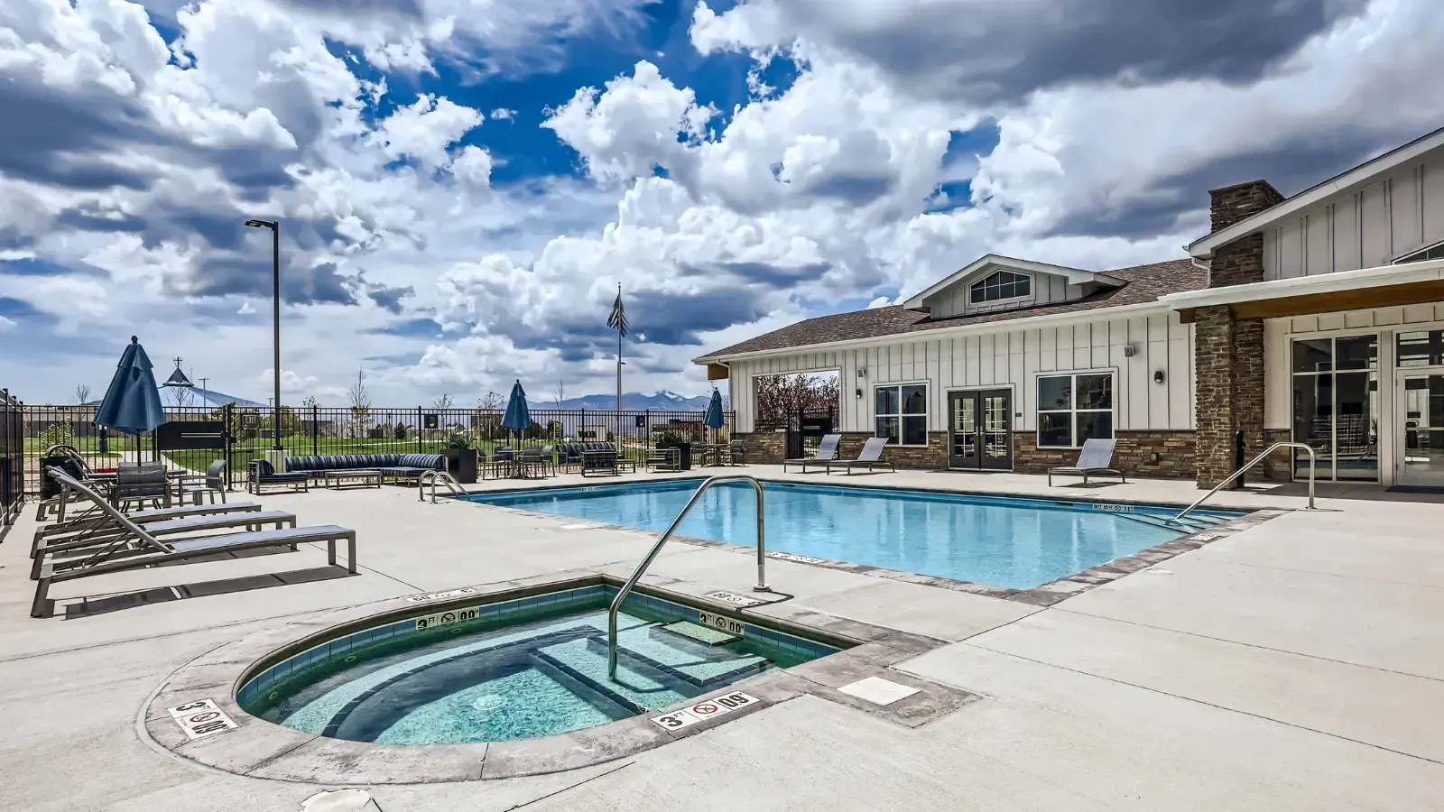 Outdoor pool and hot tub area with loungers at an apartment community.