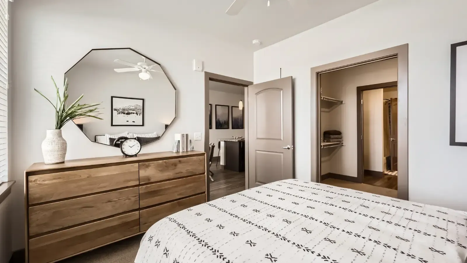 Bedroom interior with a wooden dresser, an octagonal mirror, bed, and open closet.