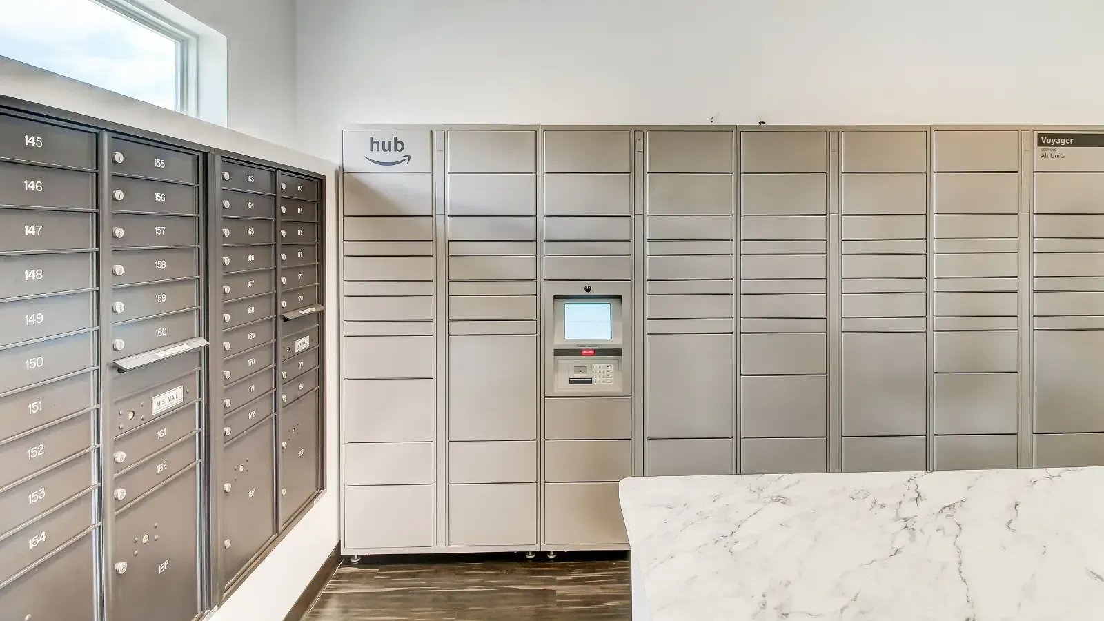 Row of gray mailboxes and parcel lockers along a wall in a modern lobby.