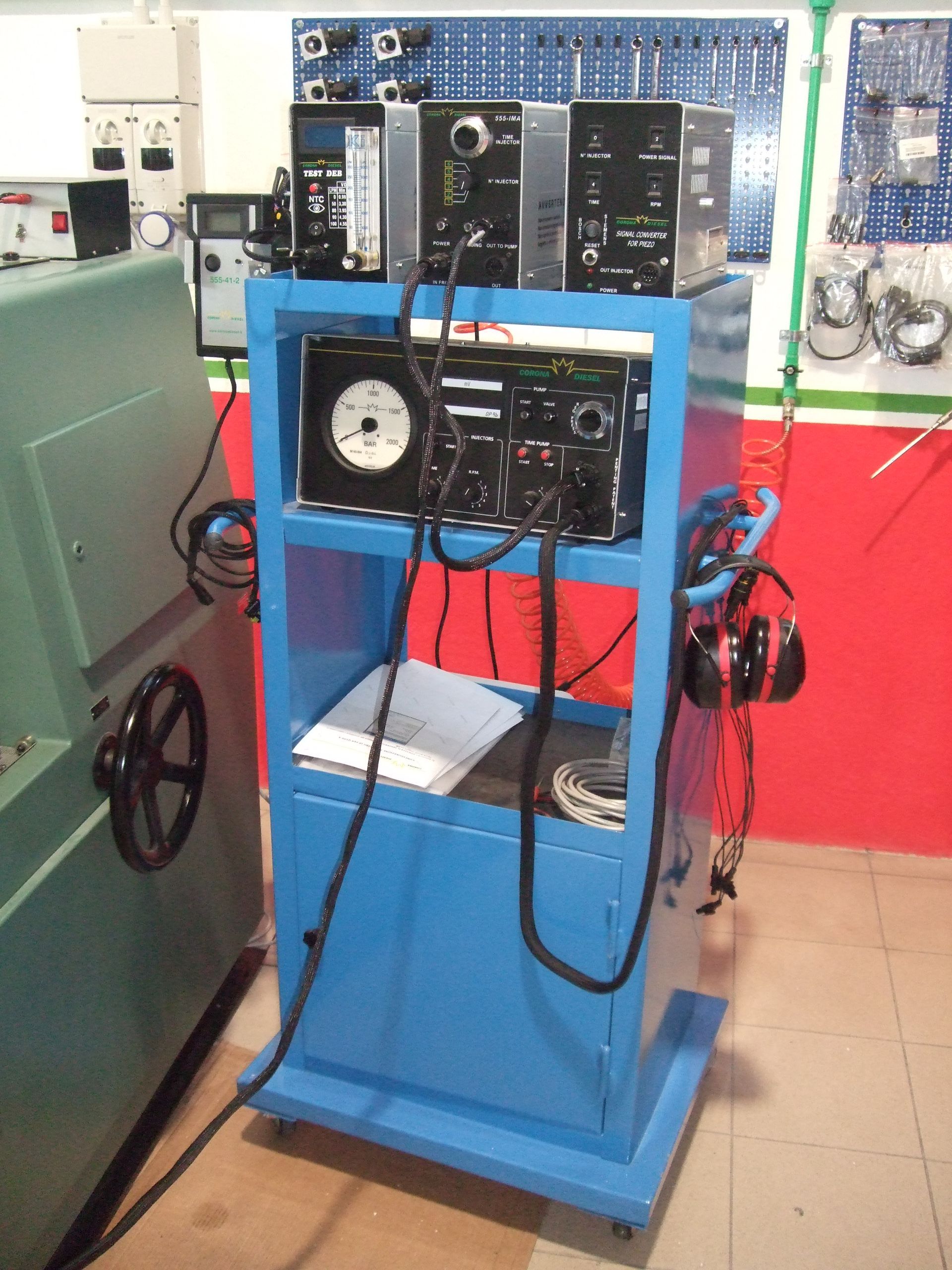 Carrello blu con apparecchiature elettroniche, cavi e cuffie in un'officina.