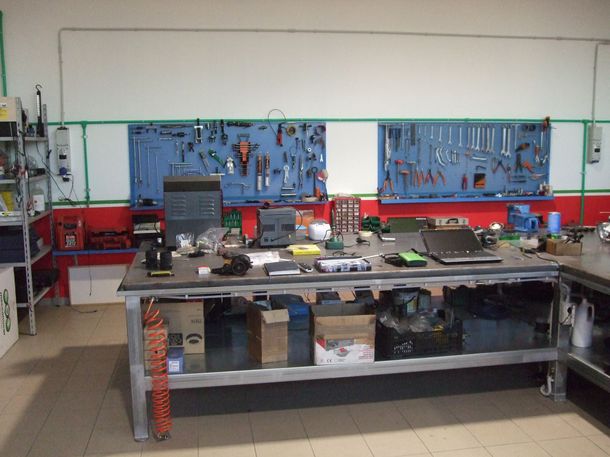 Officina con attrezzi disposti su una parete, banco da lavoro con oggetti e spazio di stoccaggio sottostante.