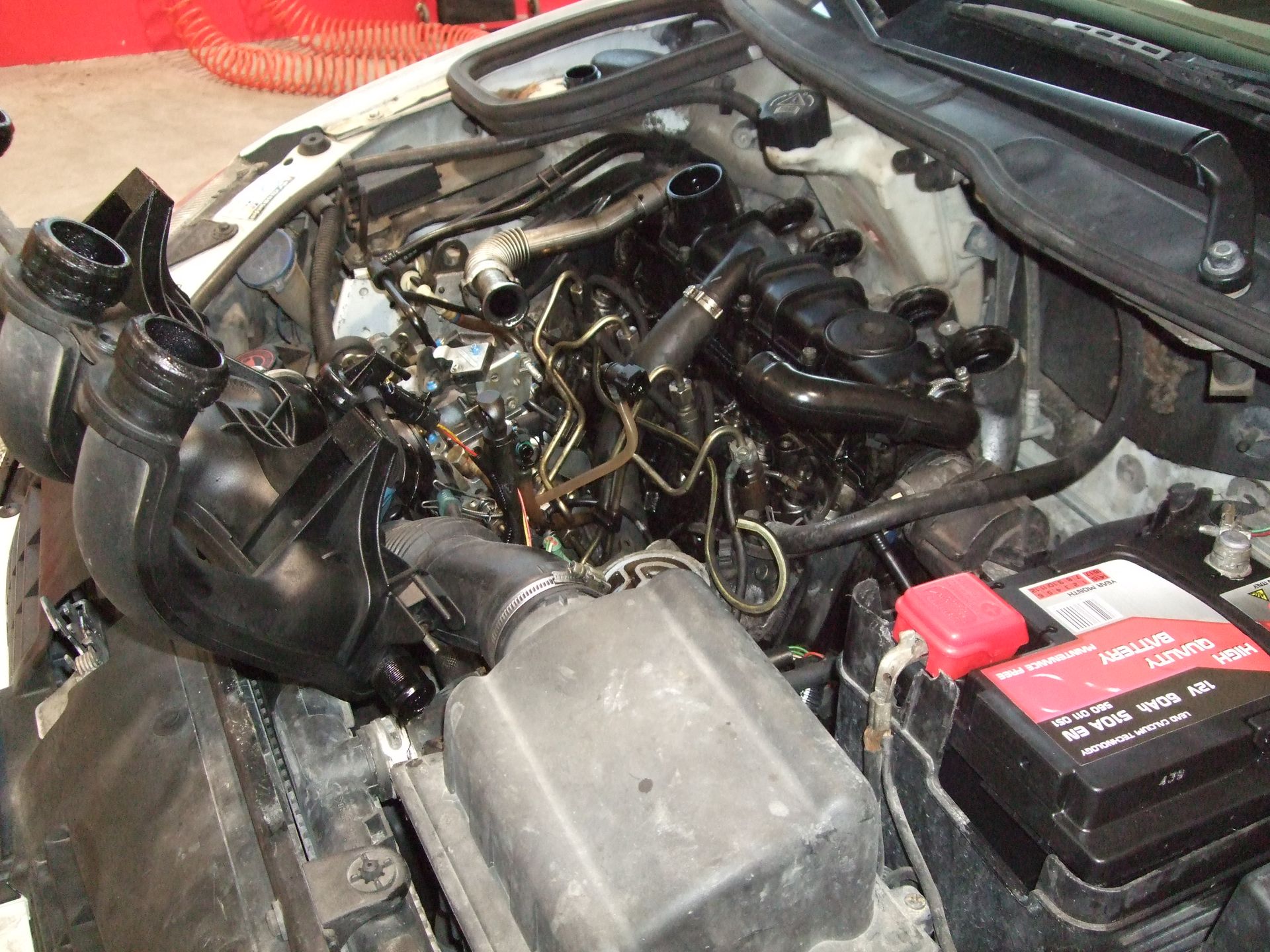 Vano motore dell'auto con filtro dell'aria e altre parti rimossi, che mostra vari componenti in uno spazio disordinato.