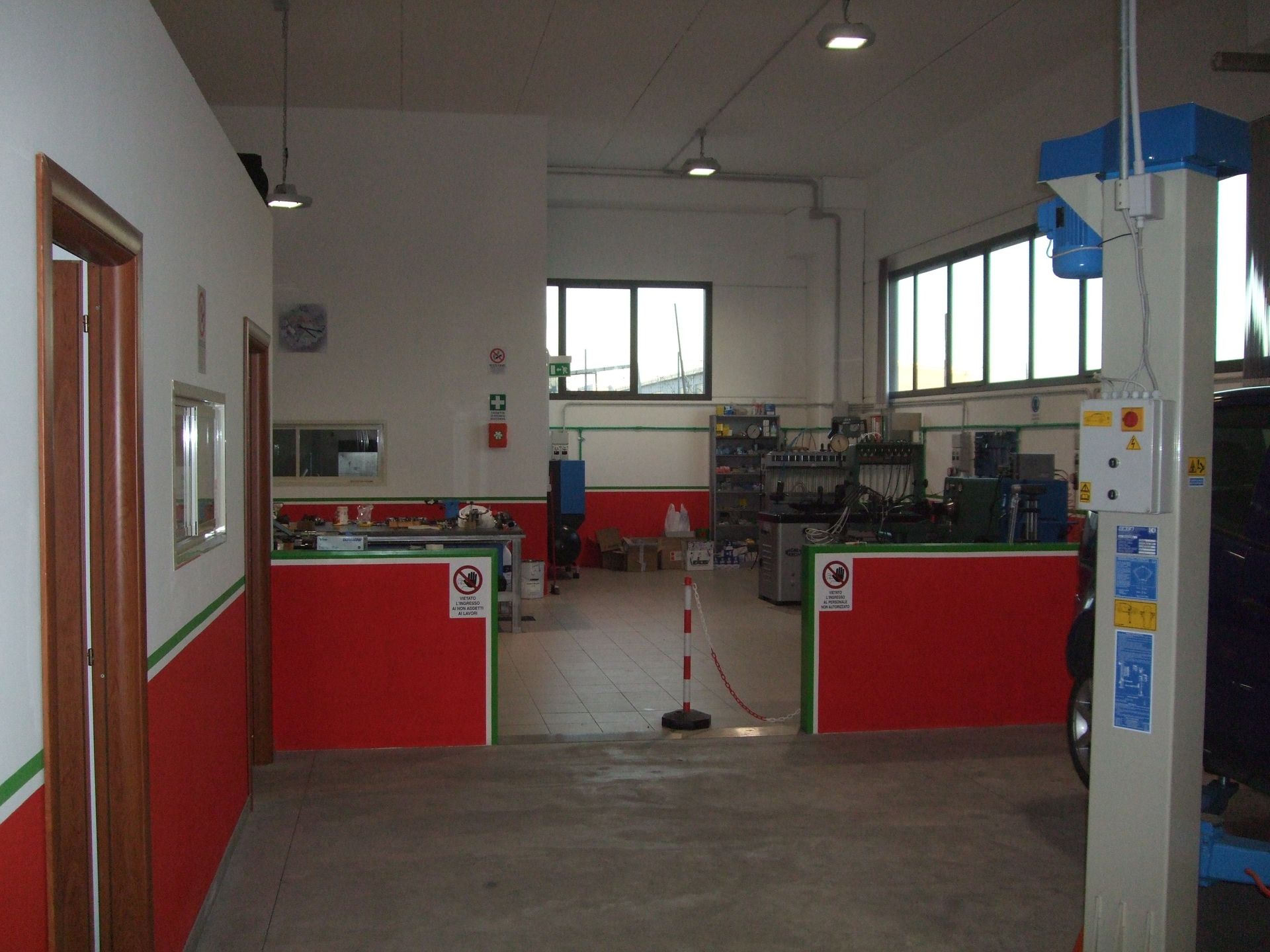 Interno di un'officina di riparazione auto con pareti rosse e bianche, attrezzi e un ponte sollevatore per auto.