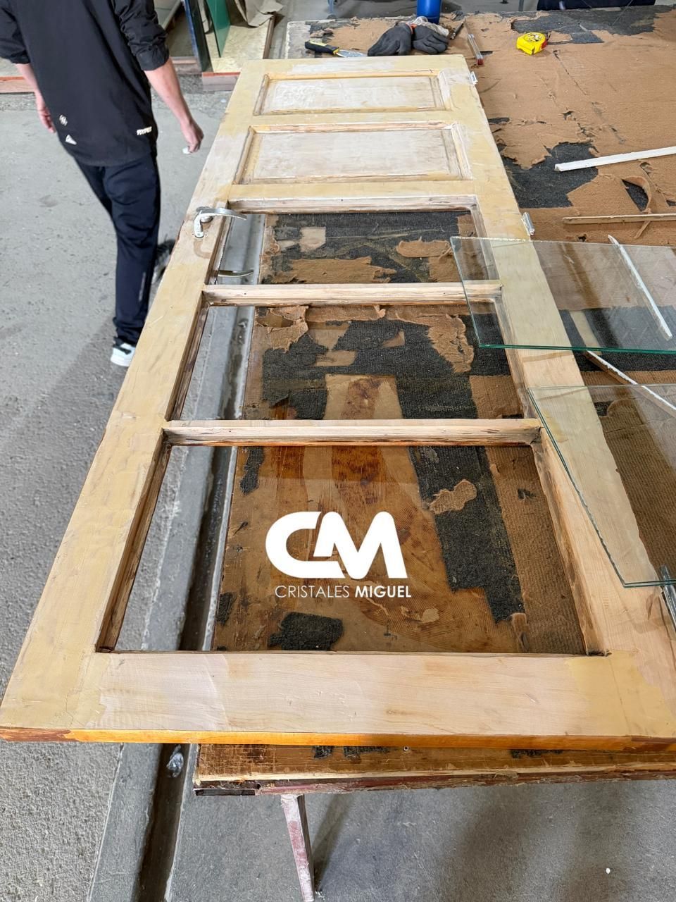 Una puerta de madera con paneles de vidrio sobre un banco de trabajo. Una persona está de pie junto a ella.