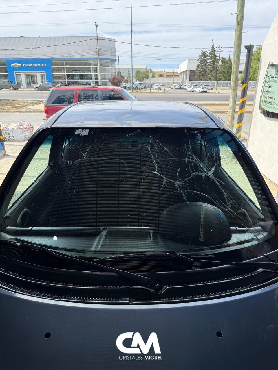 Auto con parabrisas severamente agrietado estacionado afuera de un concesionario.