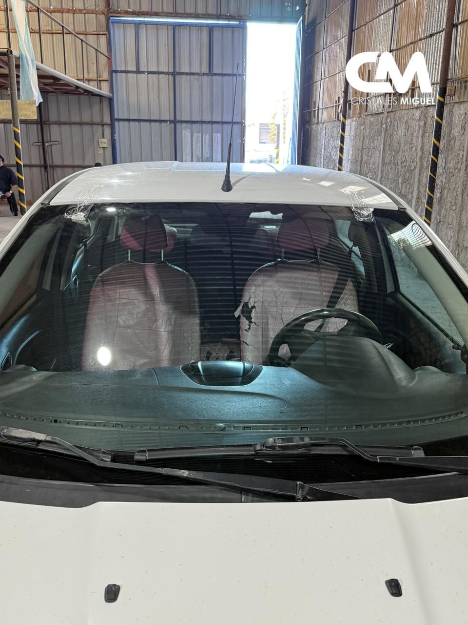 Interior de coche blanco con asientos cubiertos, visible a través del parabrisas en un garaje.