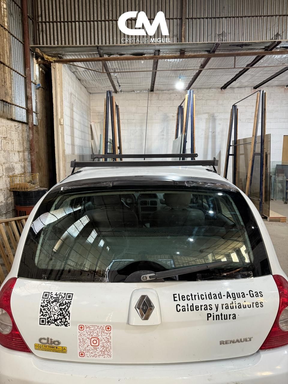 Coche blanco con portaequipajes en el techo que lleva paneles de vidrio; fondo interior de tienda.