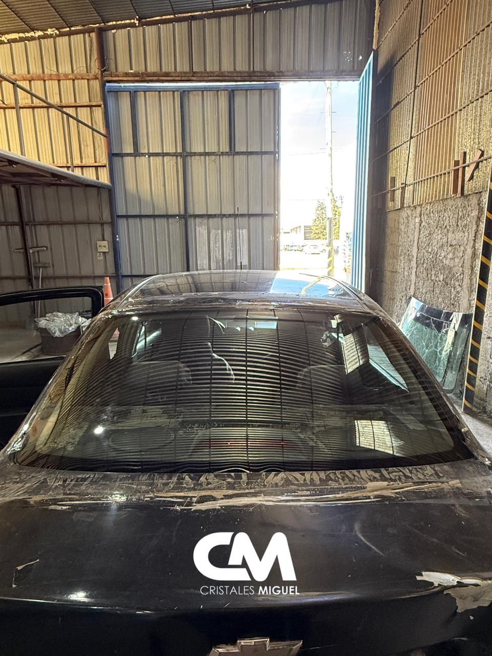Vista trasera de un coche negro dentro de un garaje; la puerta abierta revela la vista exterior con luz solar brillante.