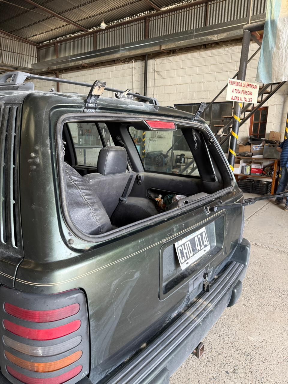 Todoterreno verde con la ventana trasera rota en un taller de reparación.
