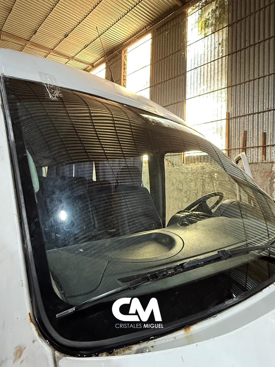 Vista interior de una furgoneta blanca con parabrisas. Se ven el salpicadero y el volante, con la luz del sol entrando a raudales.