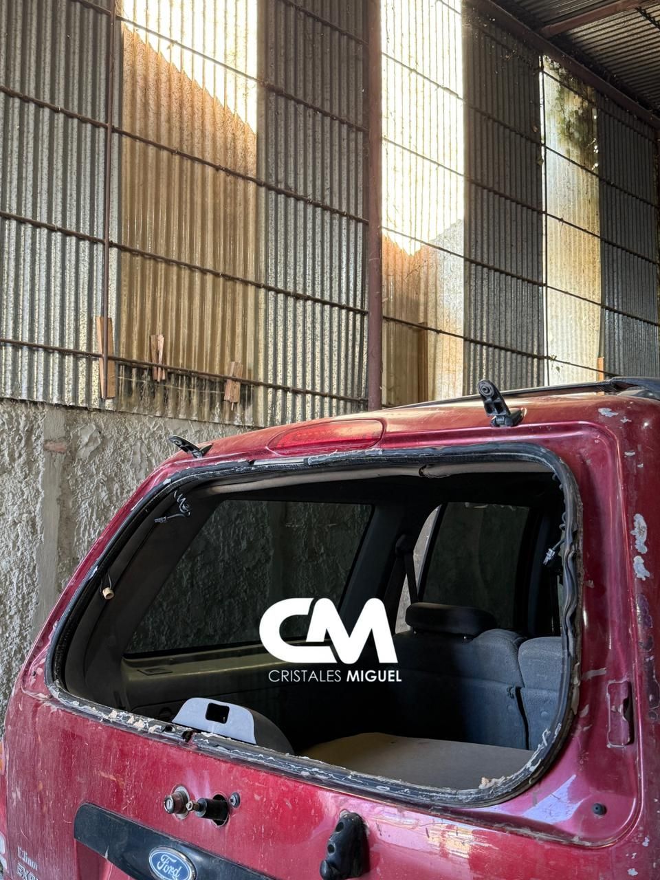 Automóvil rojo con la ventana trasera rota dentro de un edificio de chapa ondulada.