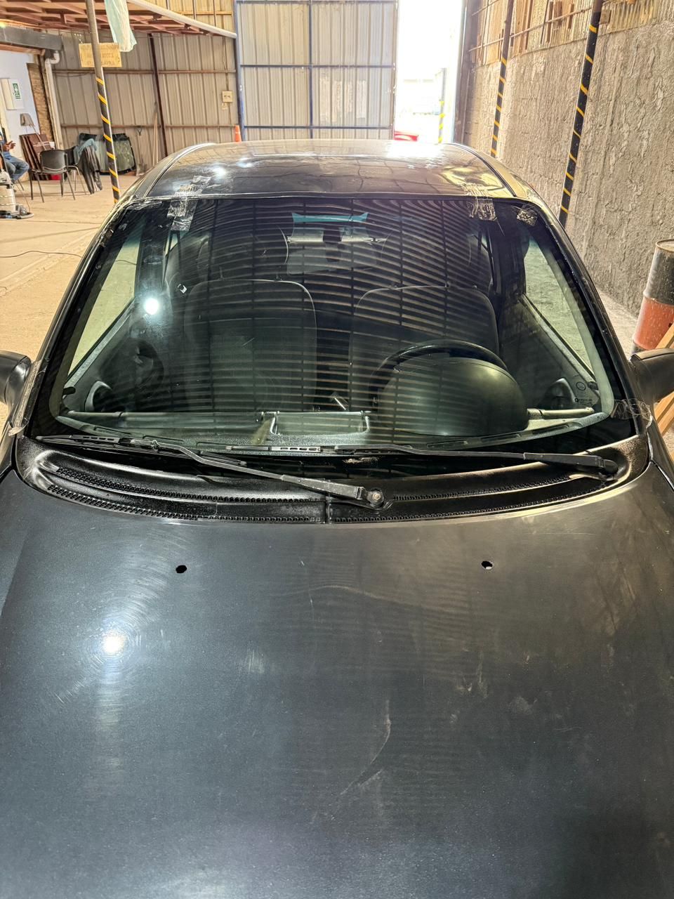 Automóvil gris oscuro estacionado dentro de un garaje, parabrisas e interior visibles.